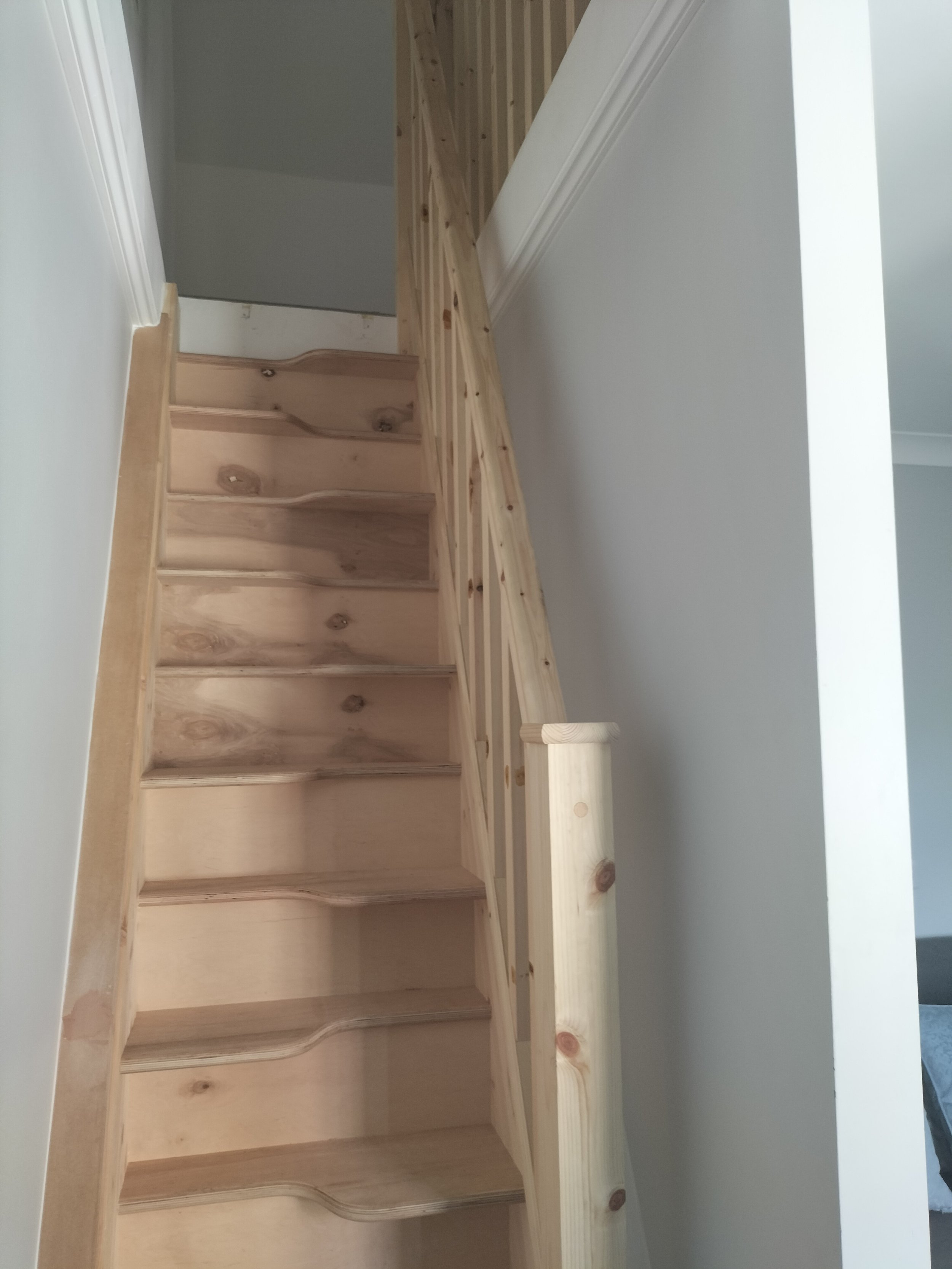 Ready to paint wooden staircase with handrail and white walls.
