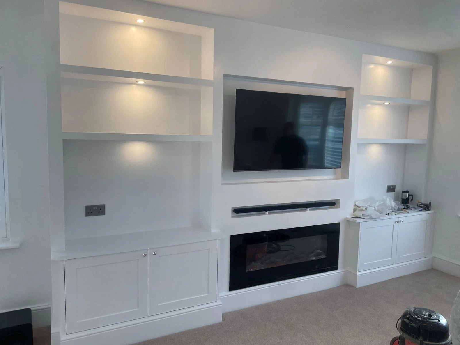 White built-in entertainment unit with open shelves, a wall-mounted TV, and an electric fireplace below the TV in a modern living room.