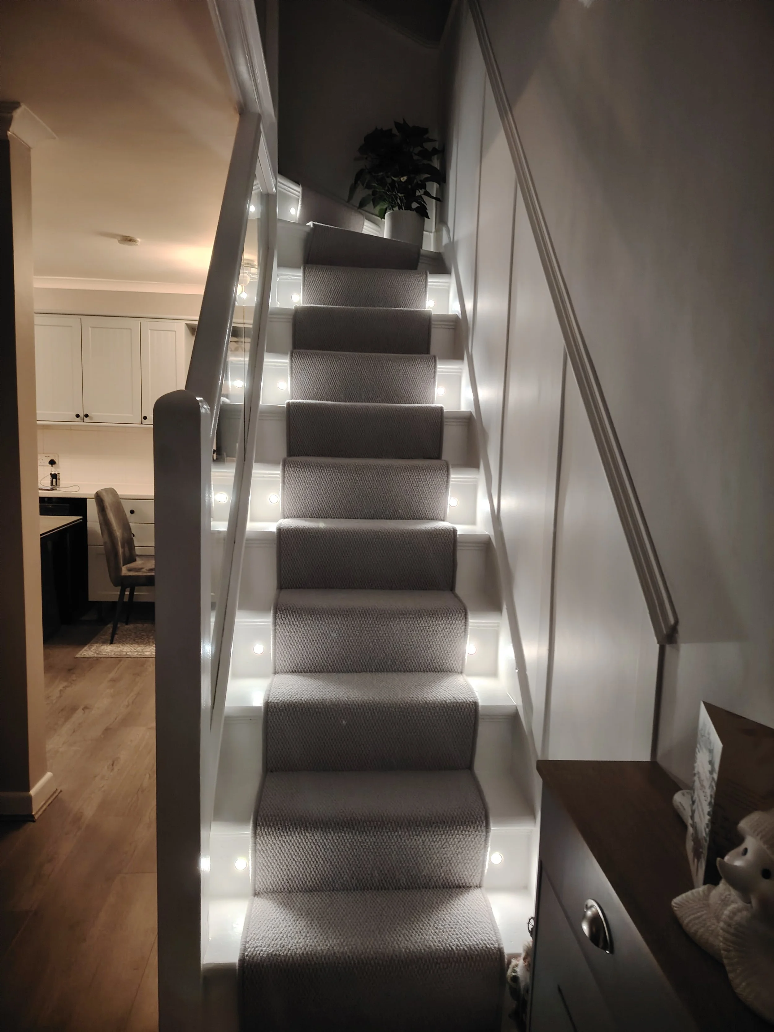 White painted stairs, grey carpet, glass balustrade, lighting