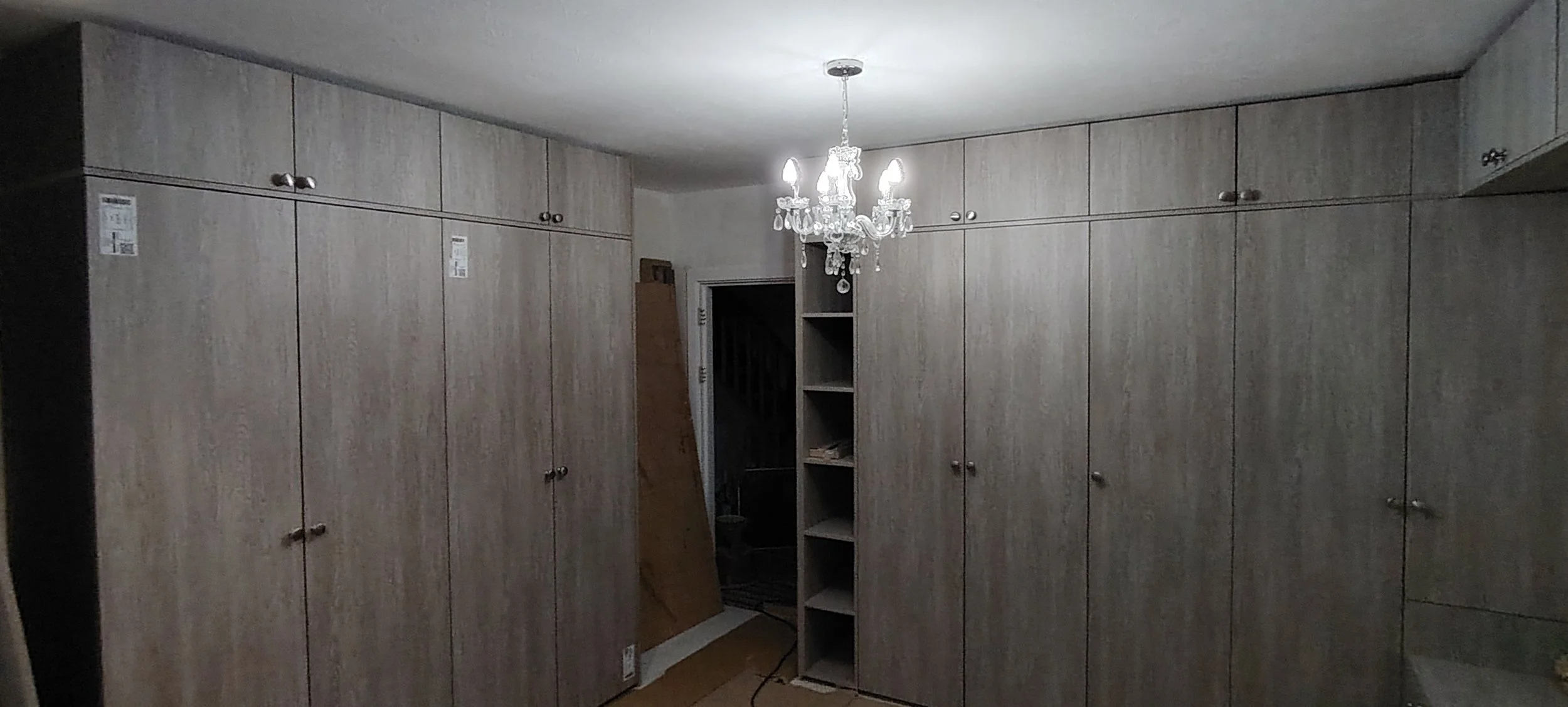 View of a room with wood-paneled closets lining the walls, a small open shelf in the corner, and a chandelier hanging from the ceiling.