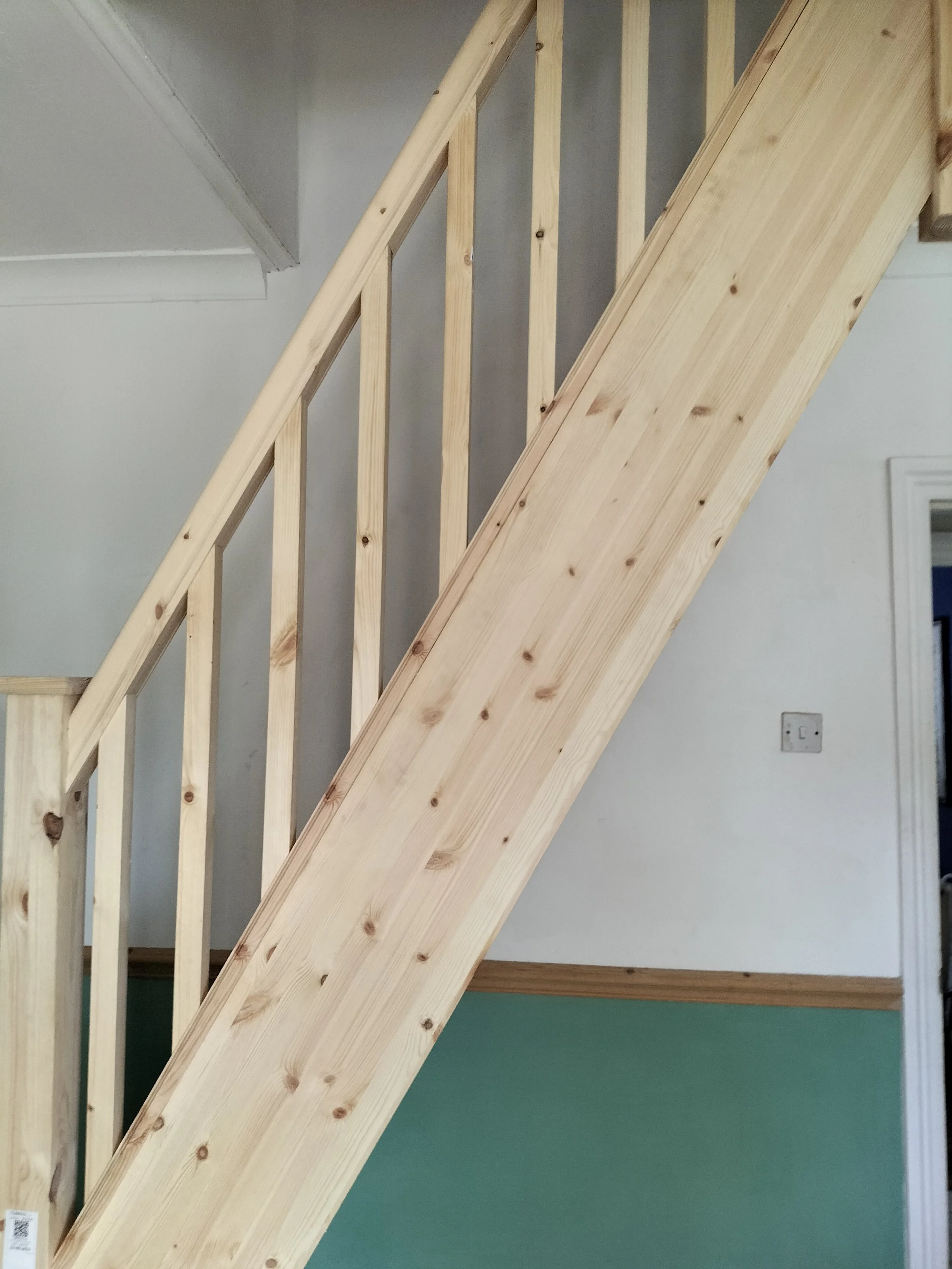 Unfinished wooden staircase with handrails, installed inside a house with light-colored walls.