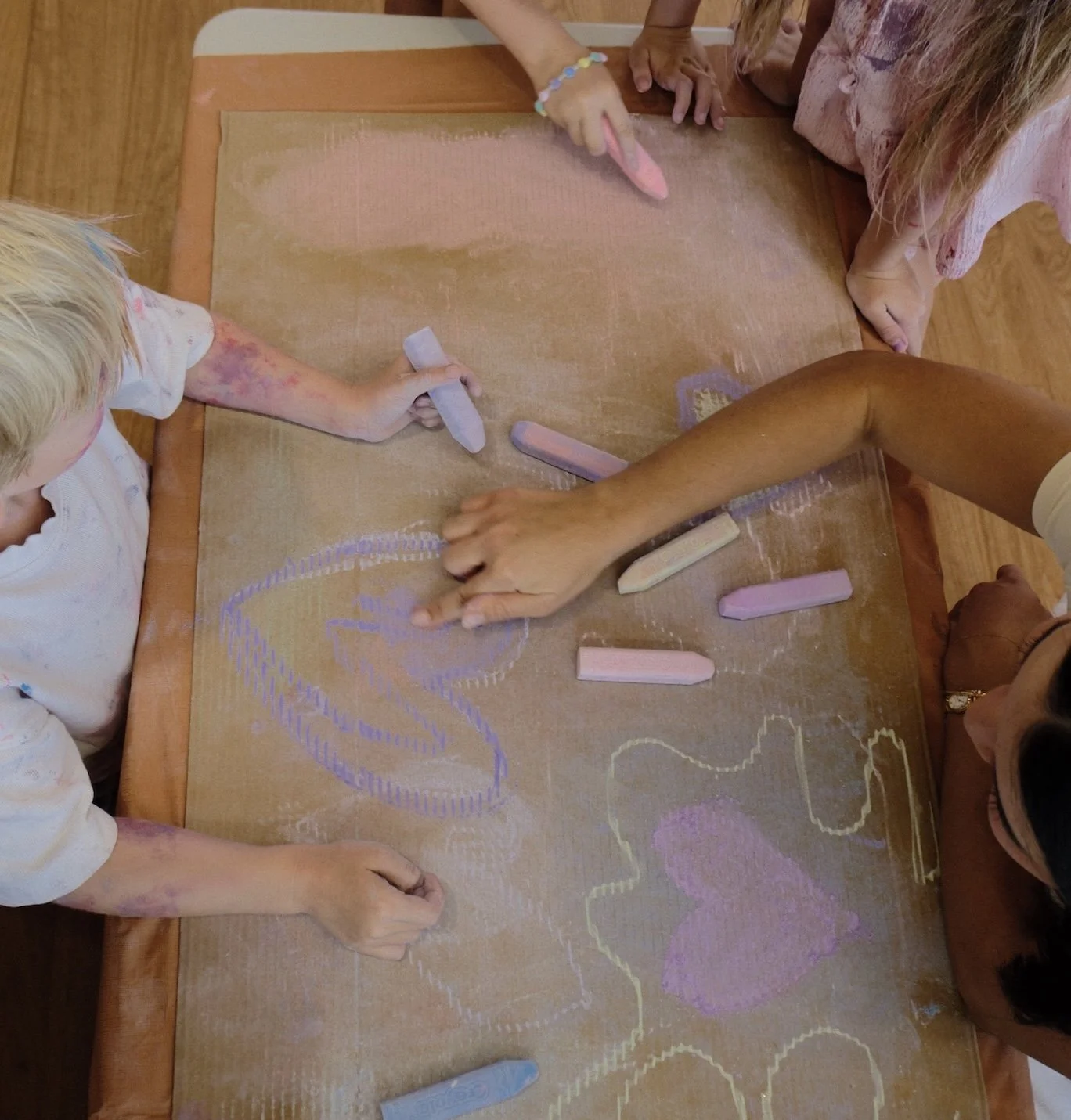 Children and an adult drawing with chalk on a large tablecloth spread on a table.