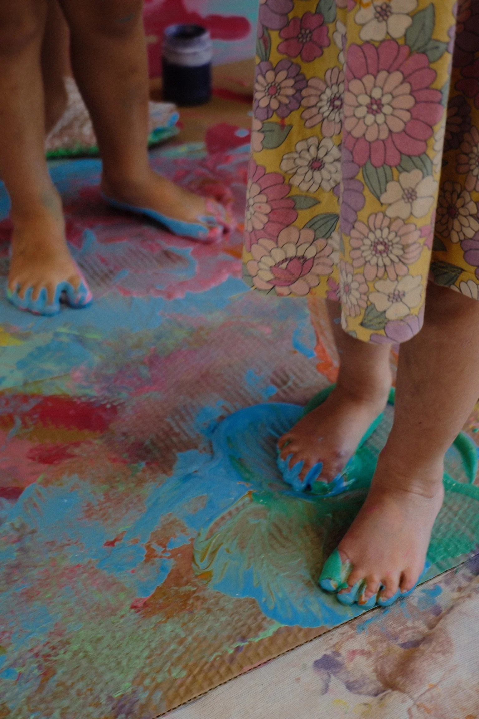 Children standing with feet on a canvas covered in colorful, mixed paint during a painting activity