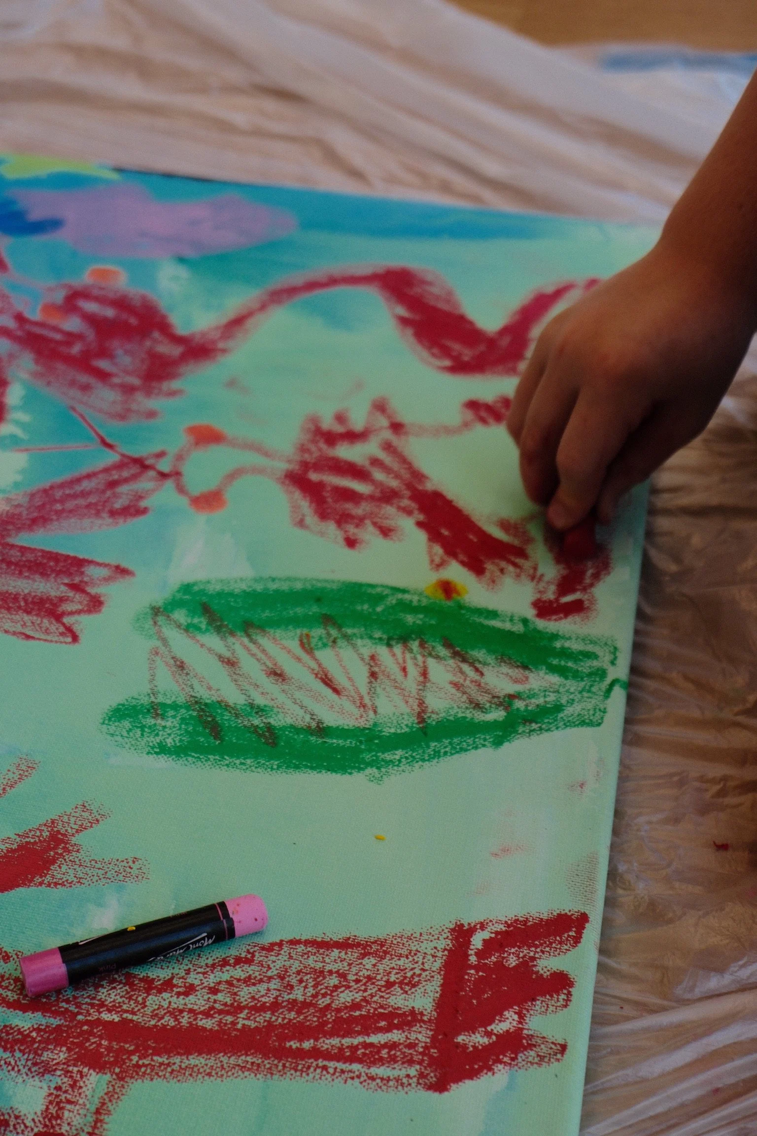 Child's hand creating a colorful abstract drawing with crayons on paper.
