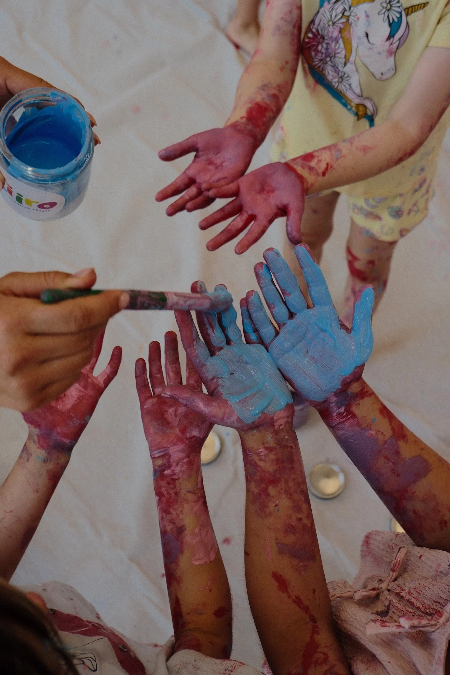 Children and adults with paint-covered hands engaging in a finger-painting activity, with blue and red paint visible on their hands.