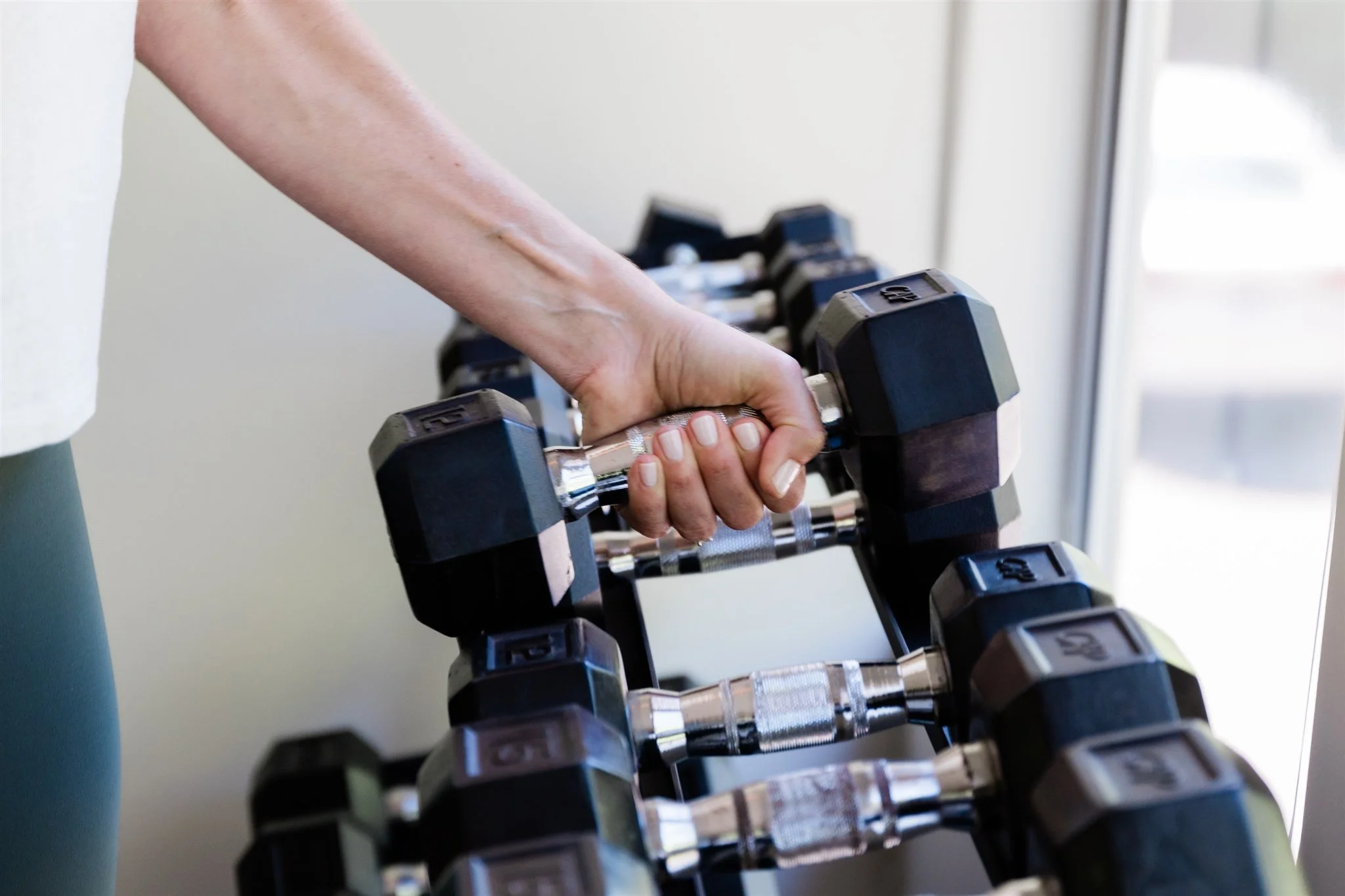 A person lifting a black dumbbell with both hands in a gym or fitness setting.