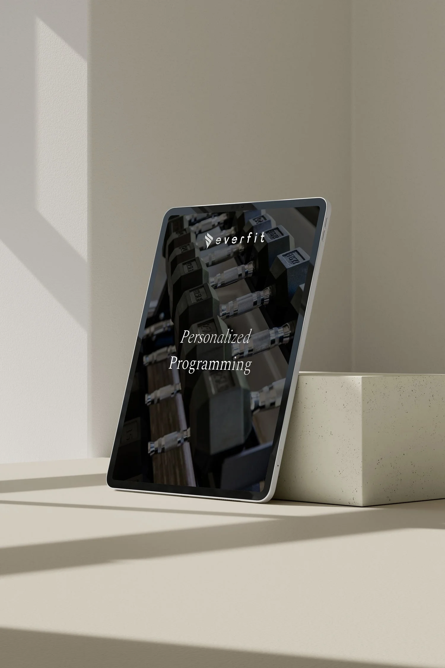 A tablet displaying an app called Everfit with a background of dumbbells and weights, sitting on a white shelf with shadows cast on a beige wall.