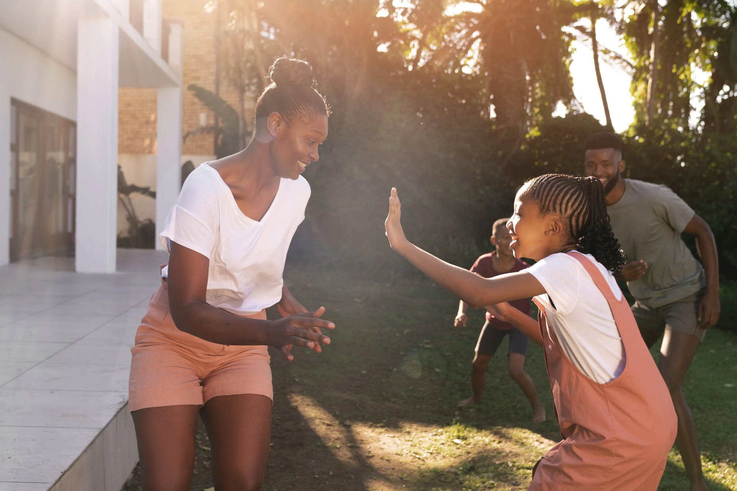 A woman and a girl are playing outdoors at sunset, high-fiving each other, with two other people in the background.
