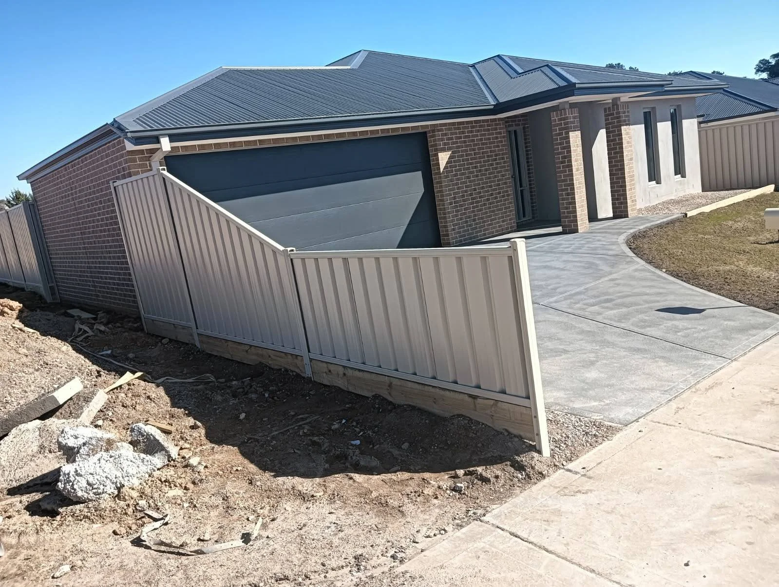 Newly built single-story brick house with a metal roof, driveway, and a metal fence in the front yard.