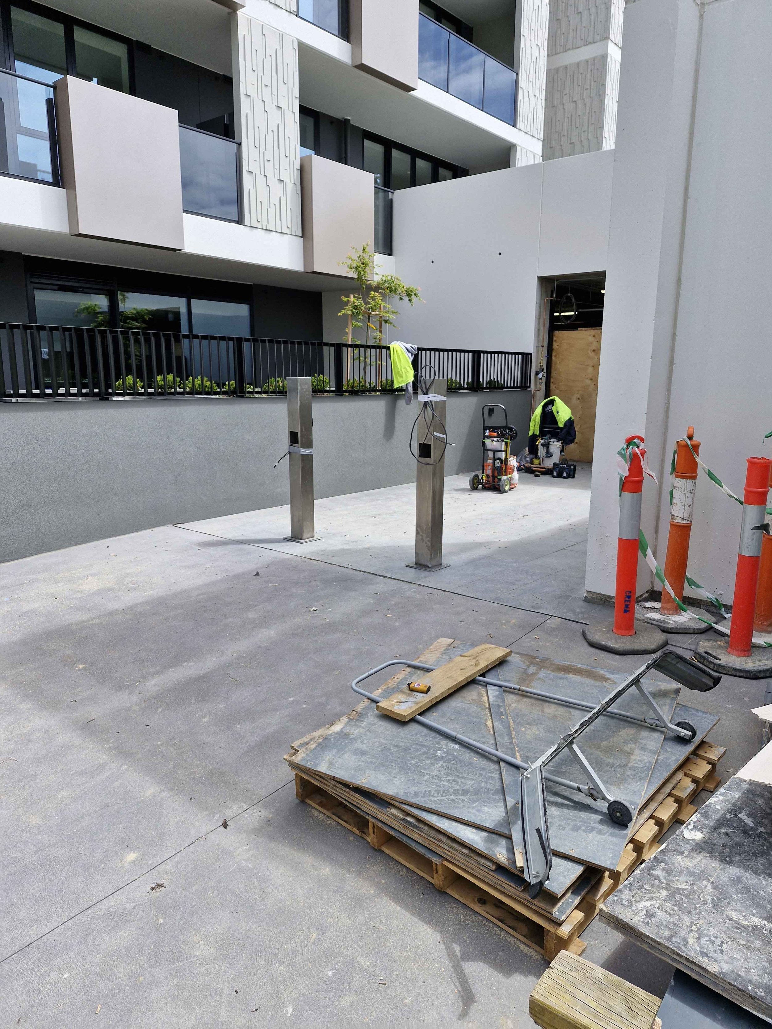 Construction site with safety cones, a hand truck on pallets, and equipment in front of a modern building.