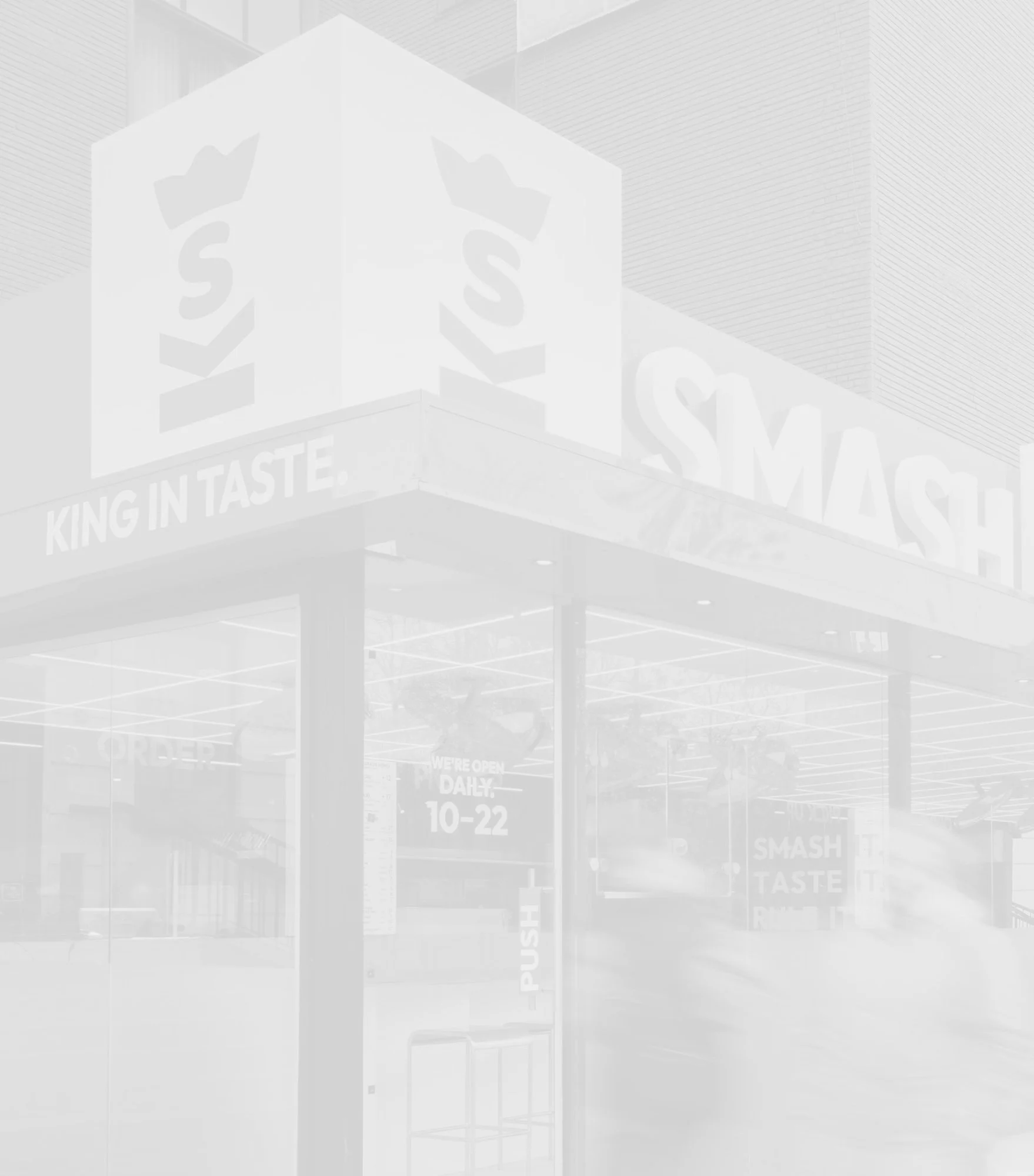 Exterior of a Smashburger fast food restaurant with signage displaying the brand's logo and slogans, including 'King in Taste.' and operational hours 10-22.