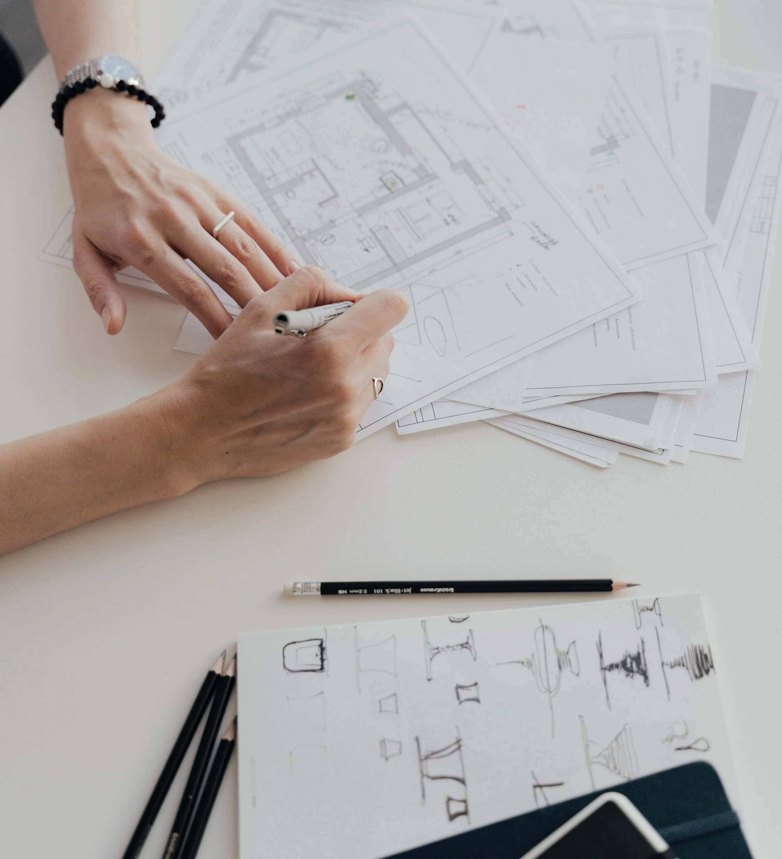 A person working on architectural floor plans at a white table, with pencils and sketches nearby.