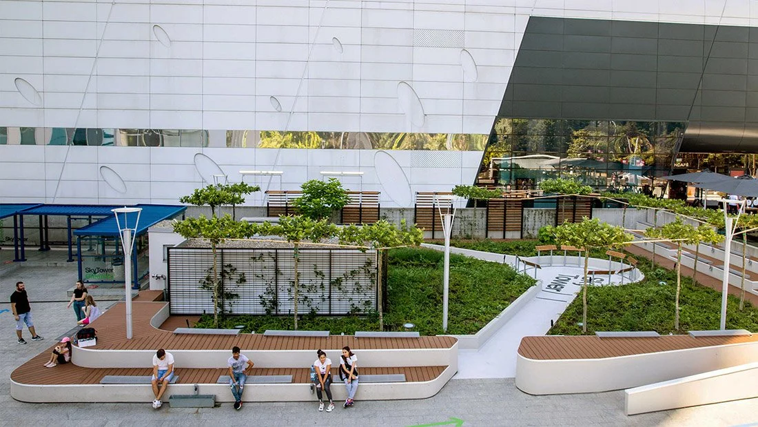 Spațiu urban SkyTower Greenery cu zone de ședere și vegetație integrată în București, Promenada mall pe fundal