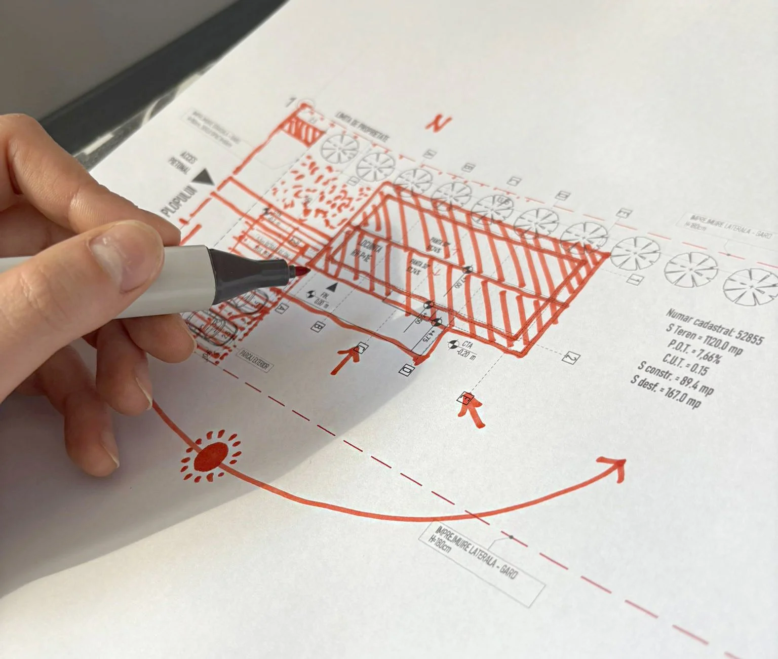 A person using a black marker to draw red lines and annotations on an architectural blueprint or site plan.