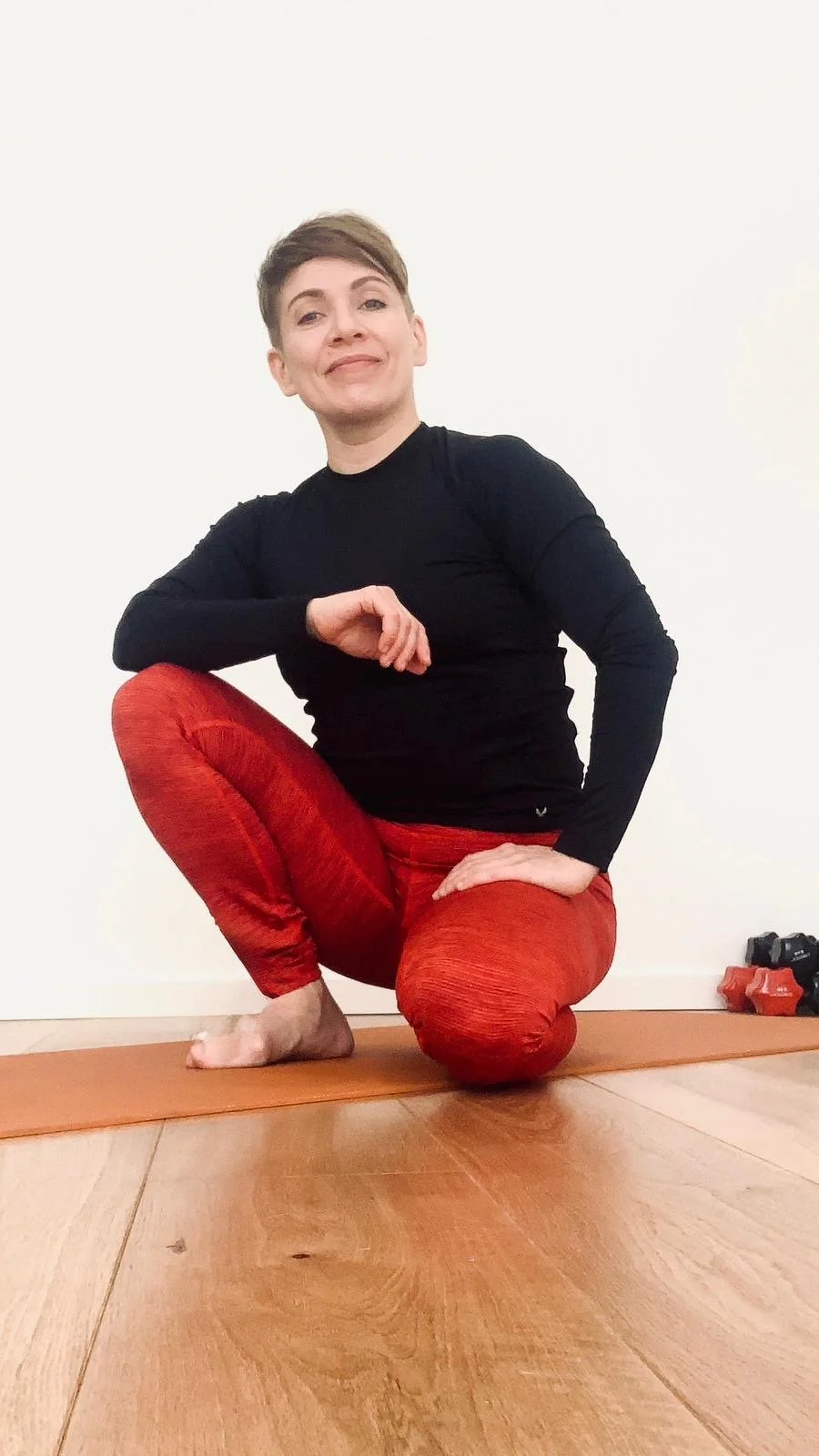 Nainen harjoittelee joogaa tai meditaatiota kulmassa, istuu lattialla ja tekee liikkeitä.