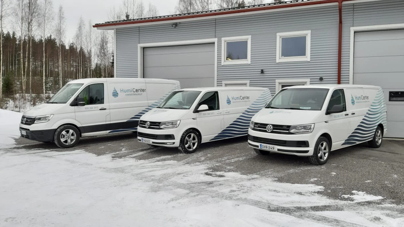 Kolme valkoista yritysautoa, joissa on HumiCenter-logo, parkissa lumisella pihalla teollisuusrakennuksen edessä.