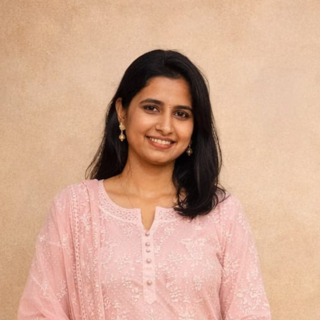 A woman with black hair wearing a pink traditional dress, standing in front of a plain beige background.