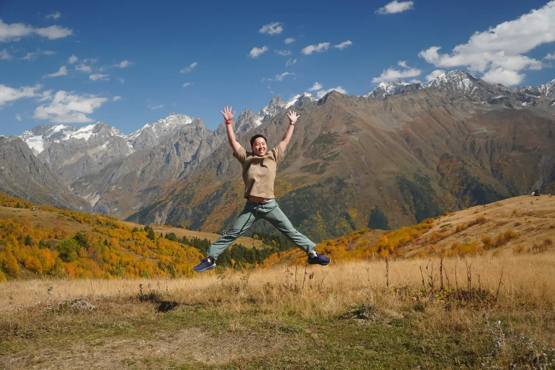 A woman jumping in the air with mountains and a clear blue sky in the background.