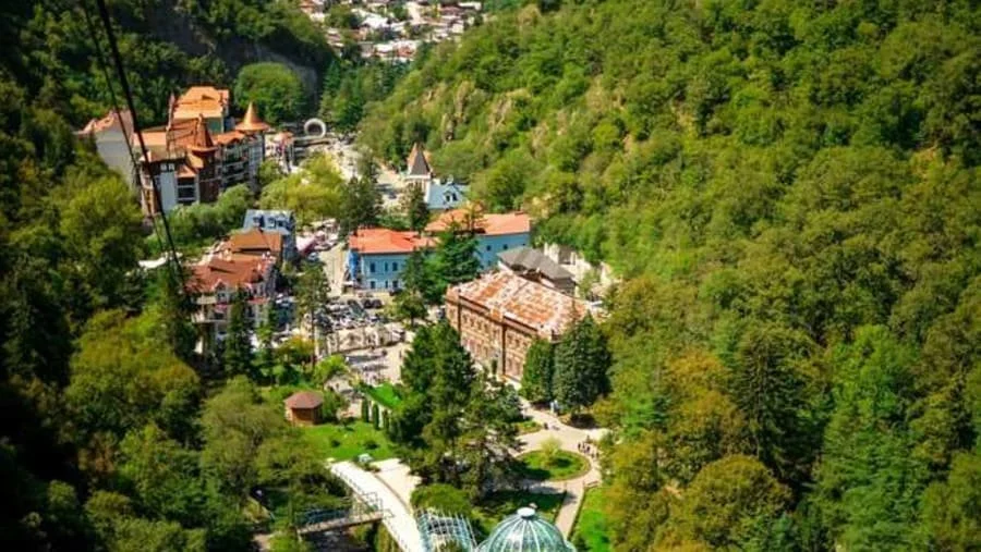 A scenic view of a small town nestled in a forested valley with colorful buildings and winding pathways.