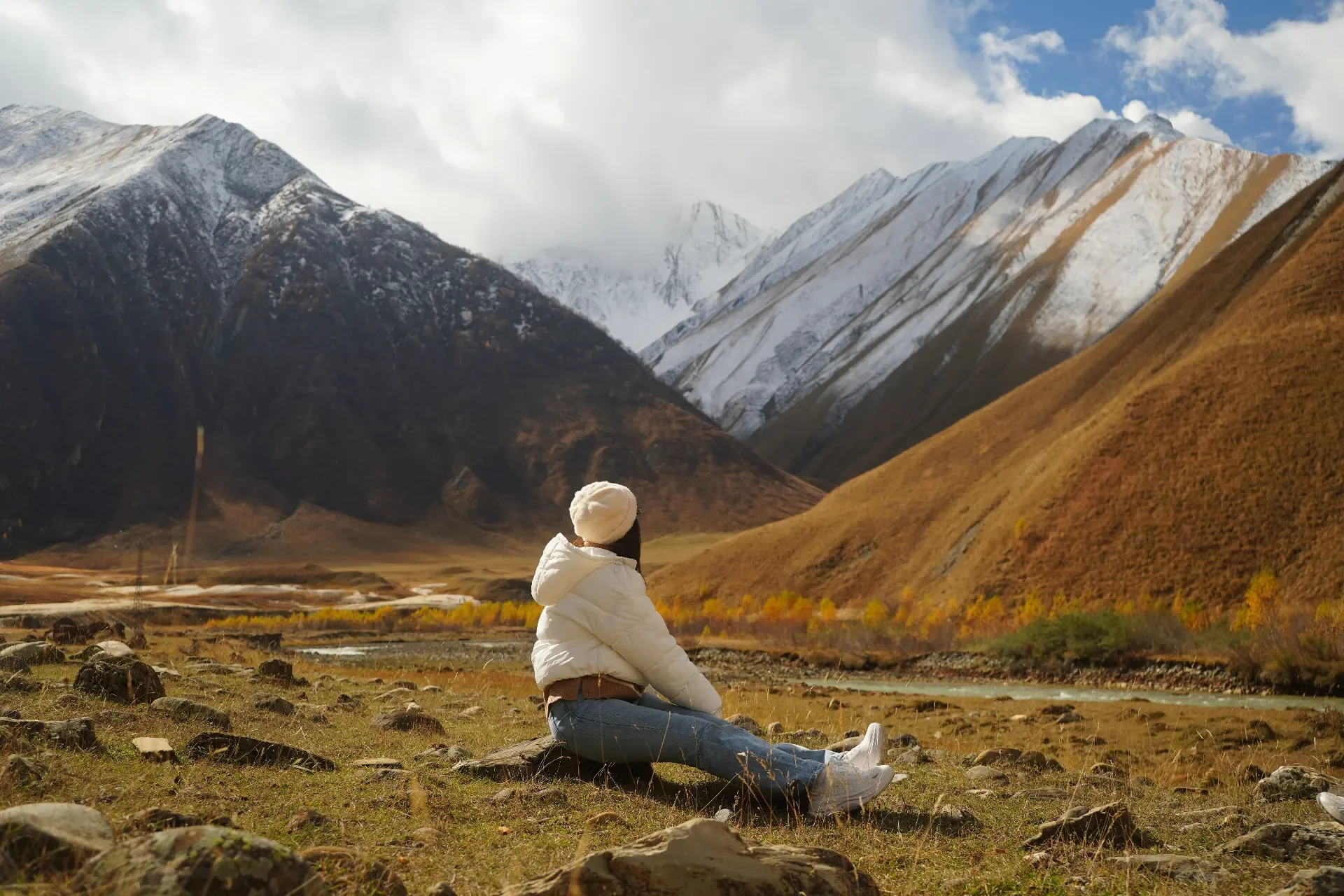 Person sitting on rocks in a valley with snow-capped mountains in the background
