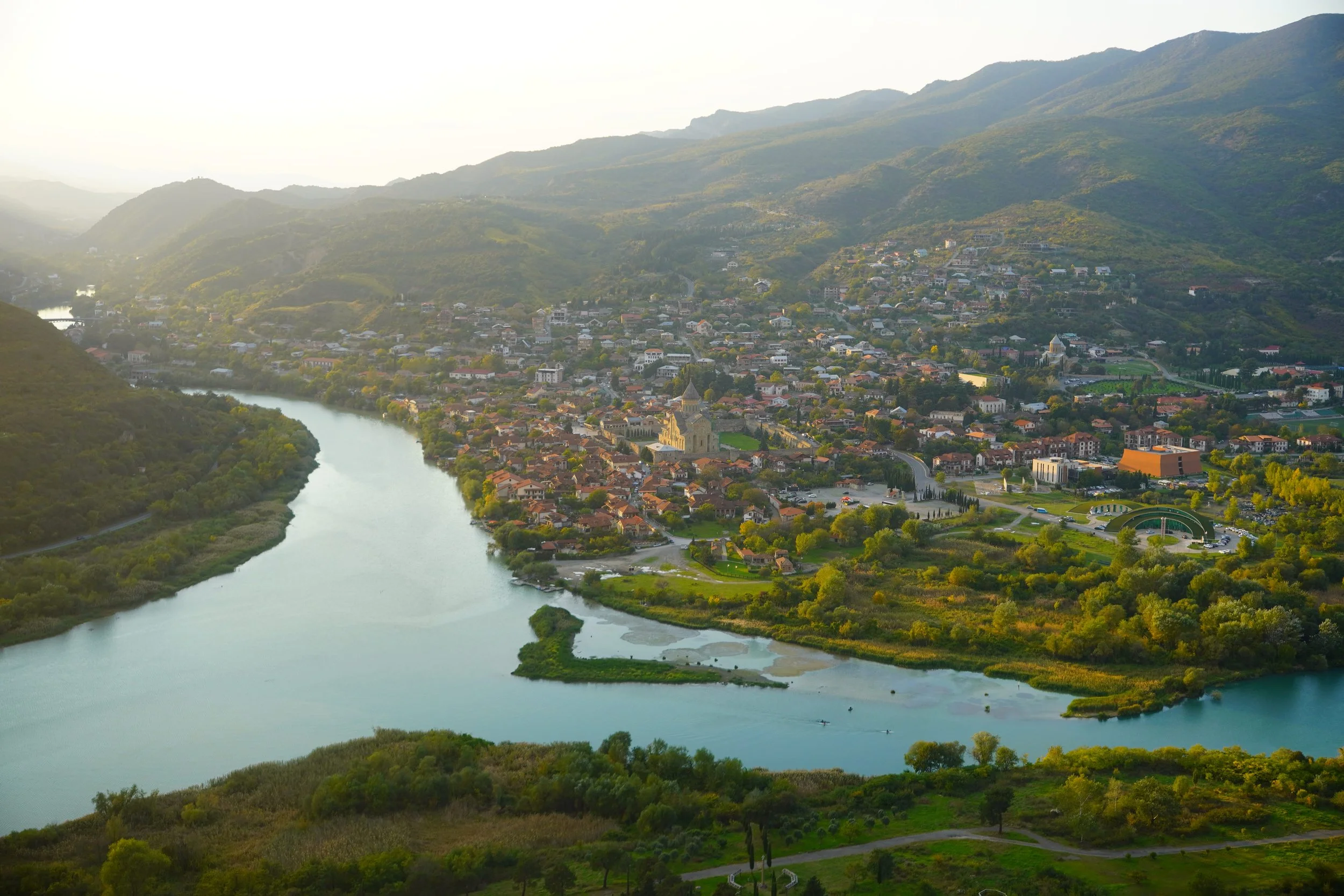 Scenic landscape of a lake surrounded by rolling hills and mountains under a cloudy sky.