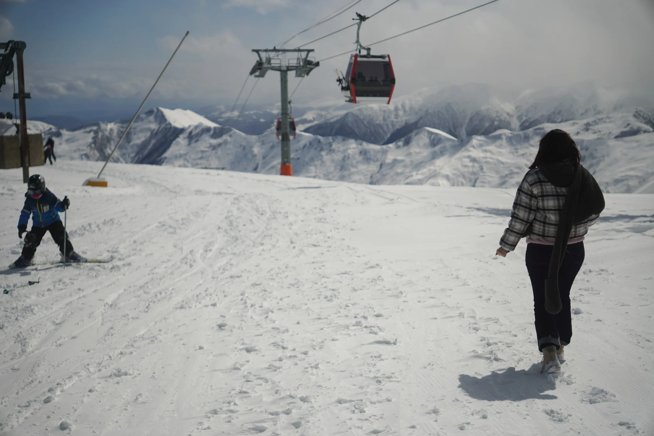 People skiing and watching snow-covered mountains with a ski lift in the background on a cloudy day.