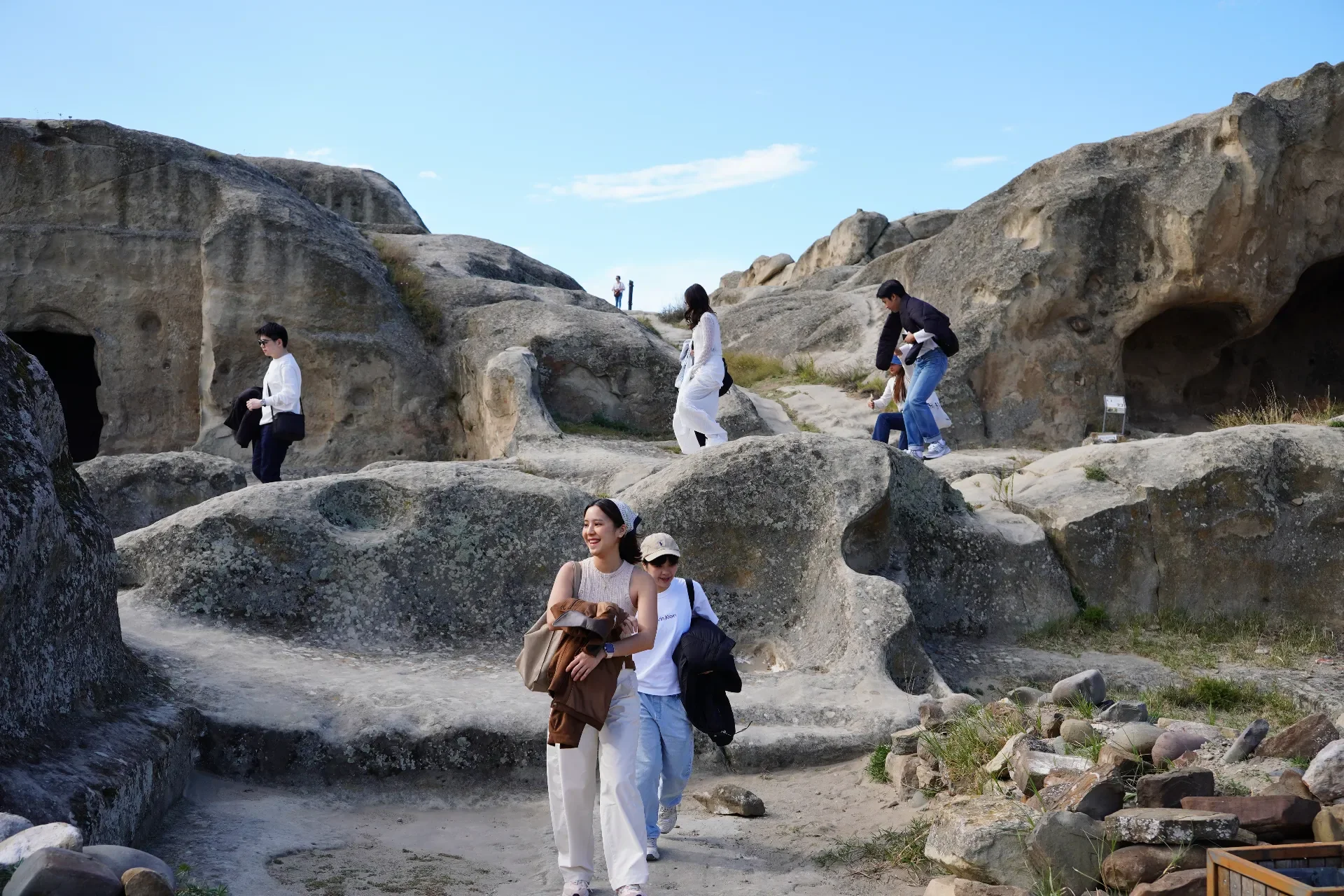 Group of people exploring a rocky outdoor area with large rocks and caves, under a clear blue sky.