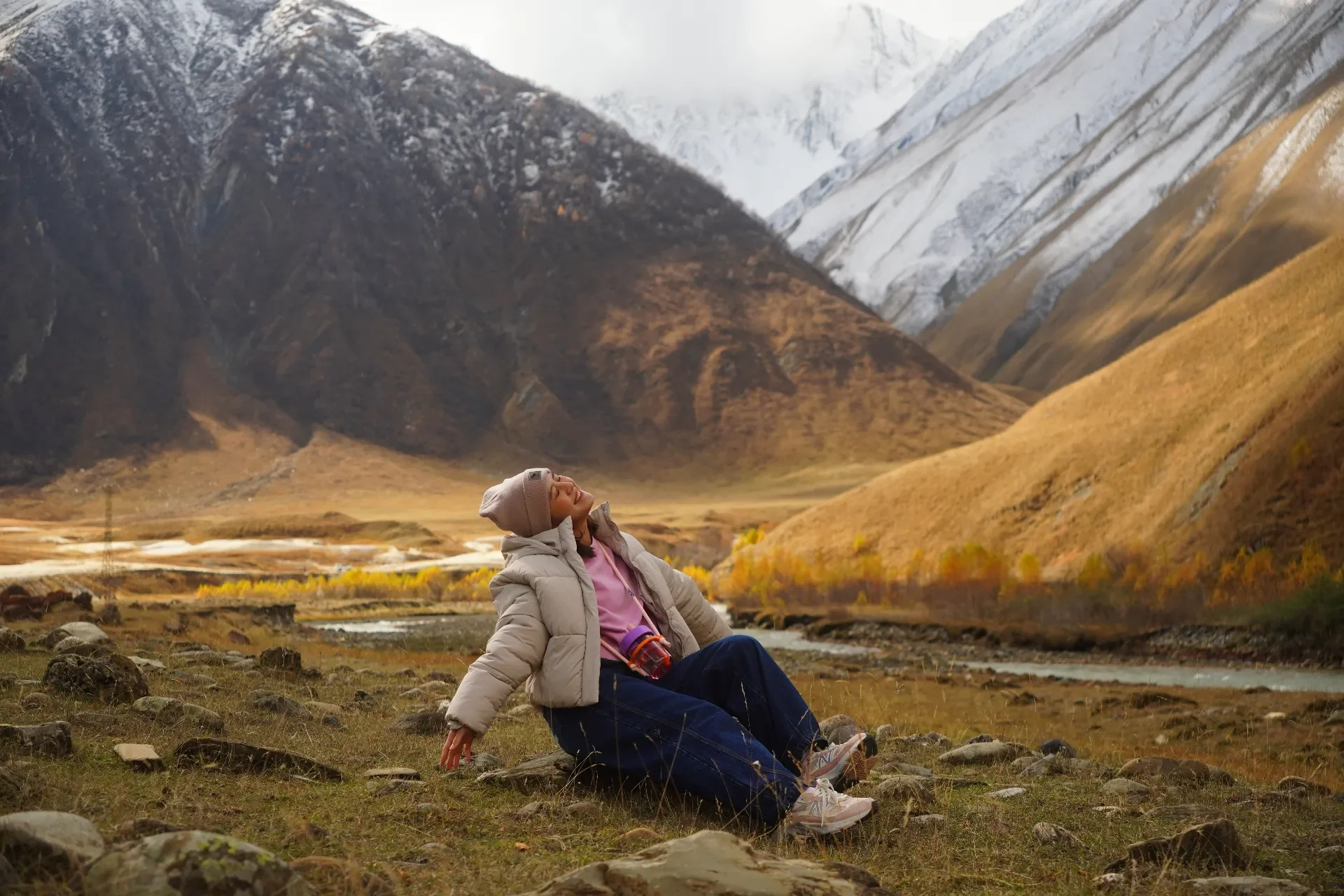 A woman sitting on rocks in a valley surrounded by mountains, enjoying the outdoors in autumn.