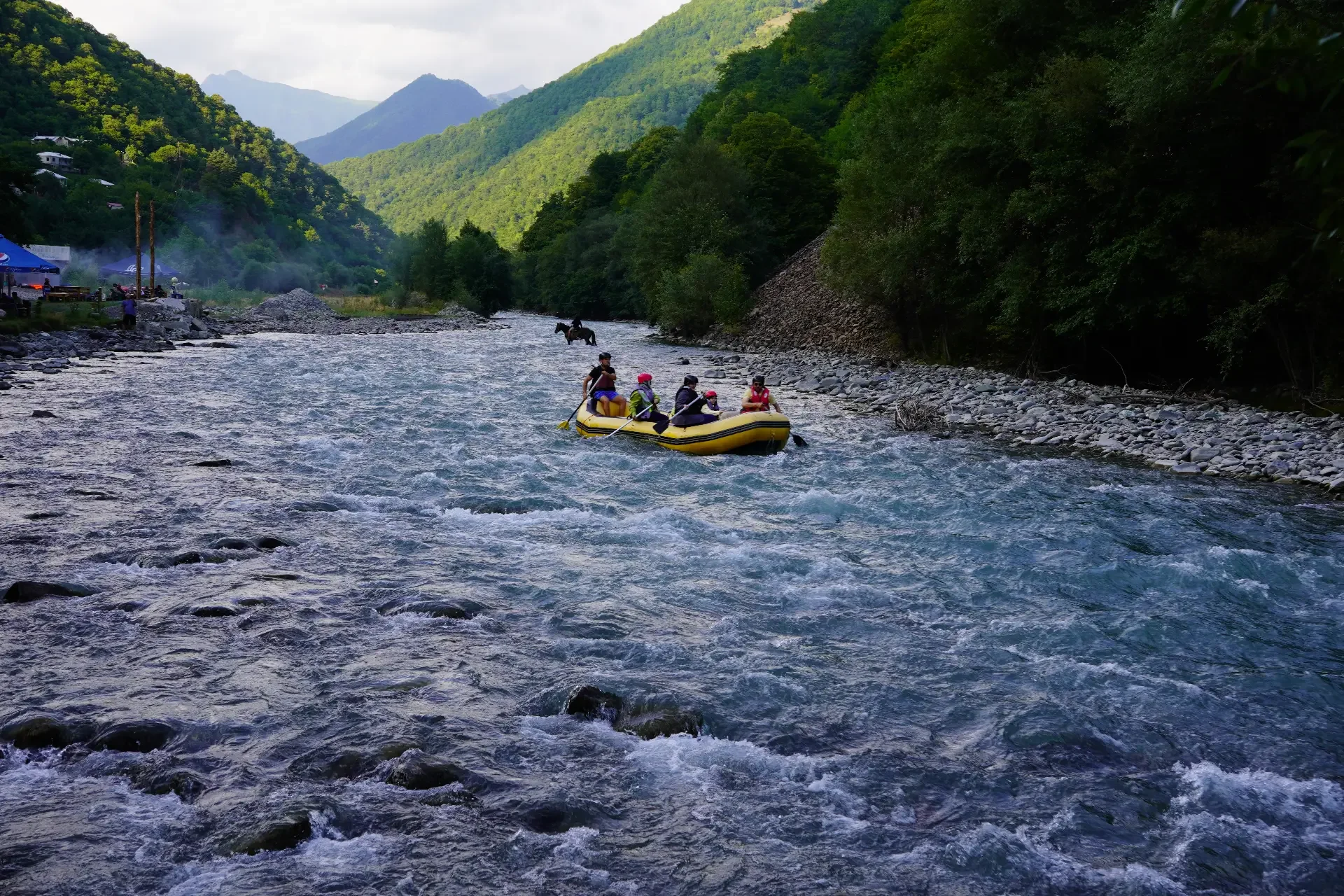 People in a yellow inflatable raft floating down a river surrounded by lush green hills and mountains.