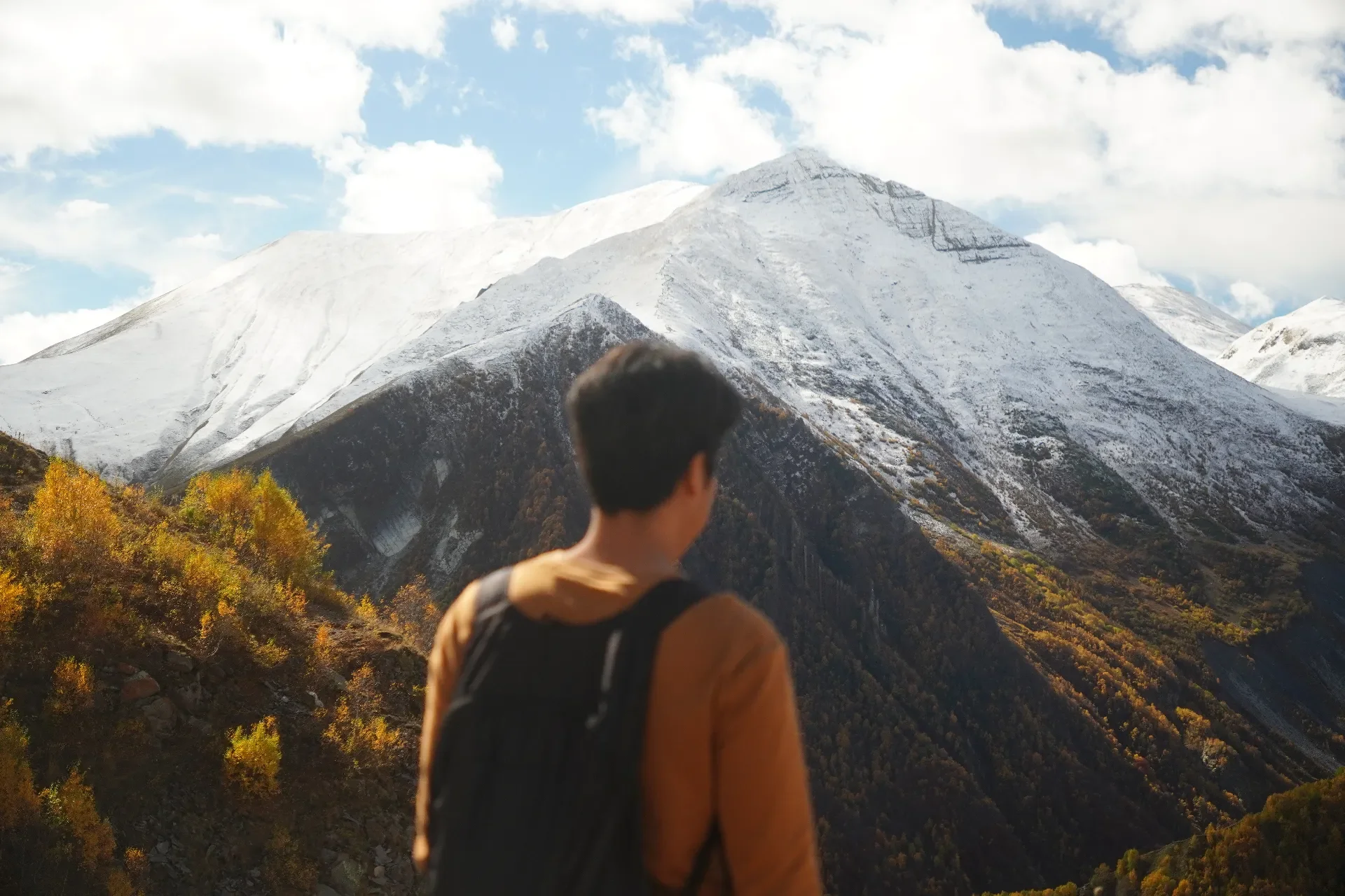 A person with a backpack looking at snow-covered mountains in the distance.