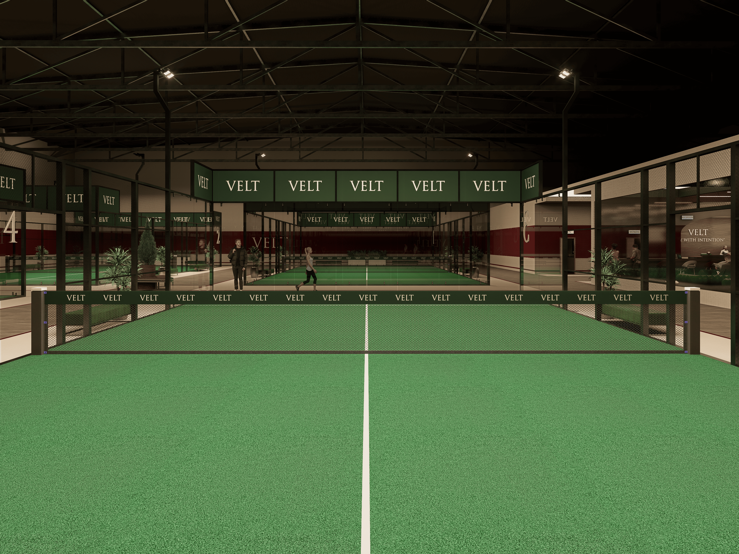Indoor pickleball court with green surface, black fencing, and VELT branding; two players on the court, sitting and walking in the background.
