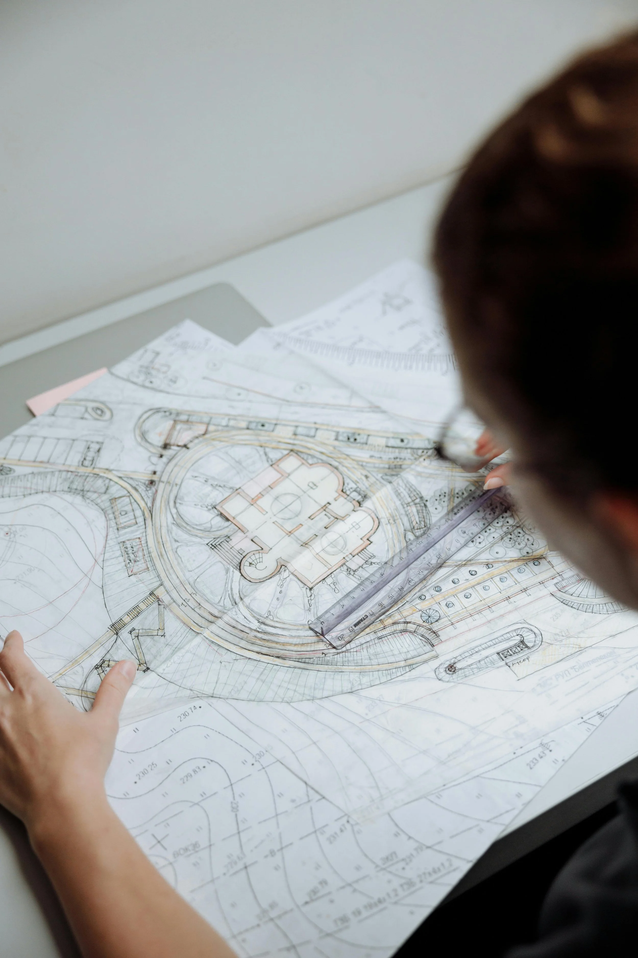 A person reviewing an architectural blueprint of a building and landscape design on a table.