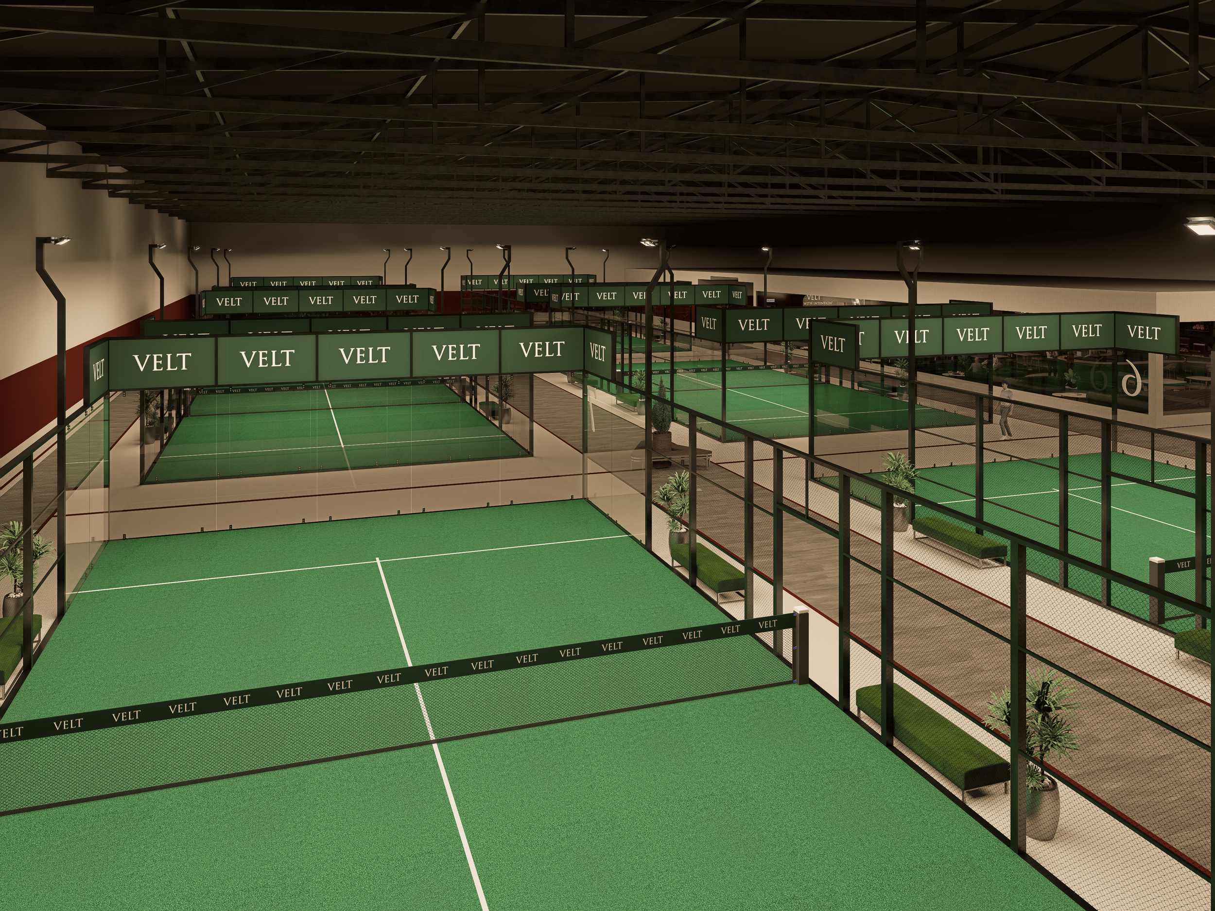Indoor tennis court facility with multiple courts, surrounded by glass fencing, benches, and potted plants, with overhead lighting and a dark ceiling.