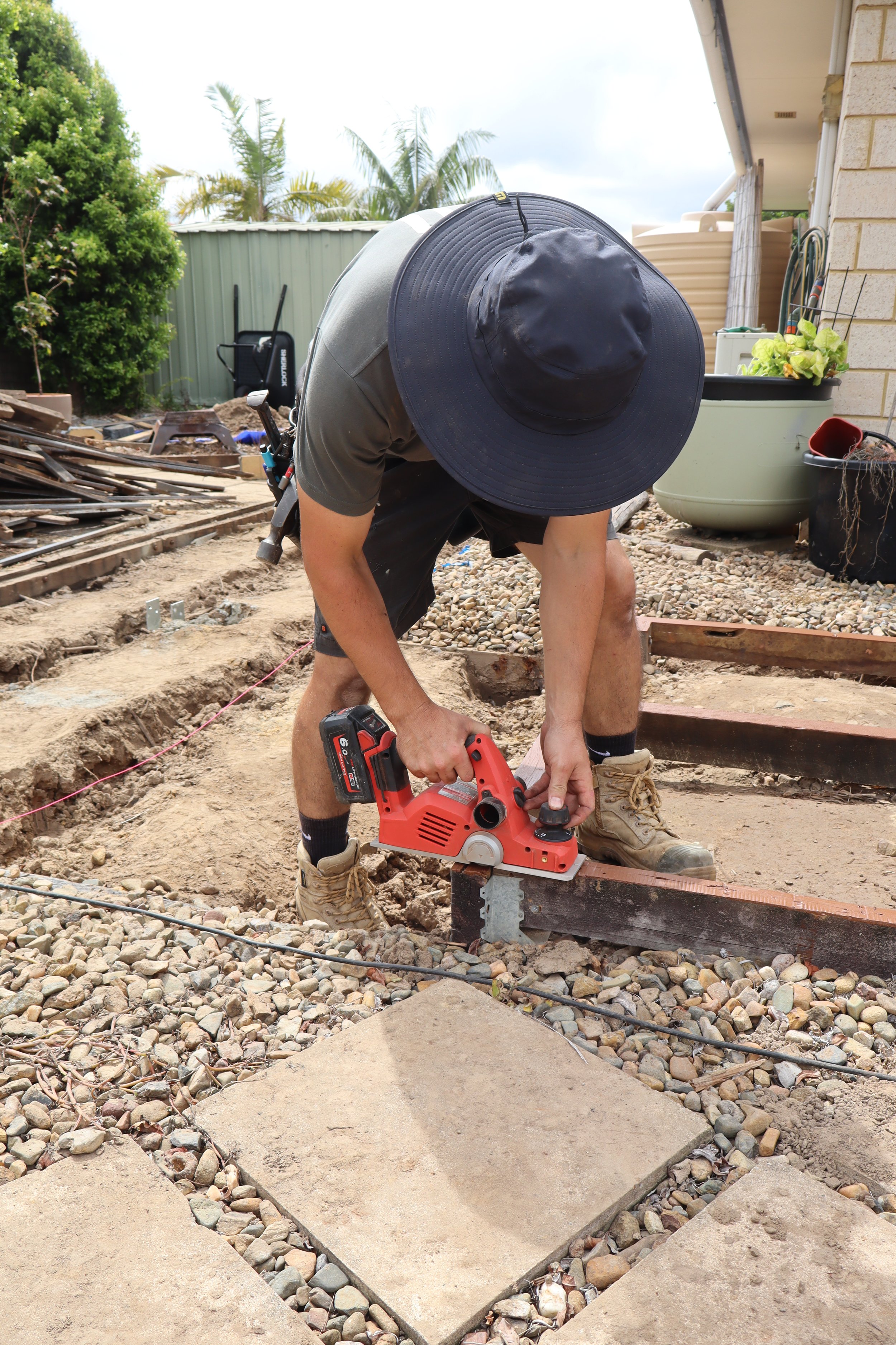 A person wearing a wide-brimmed hat uses a power tool to work on a construction site outdoors.