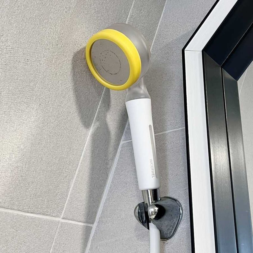A handheld shower head with a yellow and grey face, mounted on a tile wall near a glass door.