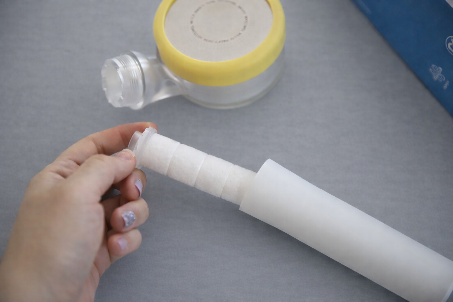 Person holding a tissue roll in front of a plastic water bottle and yellow tape roll on a gray surface.