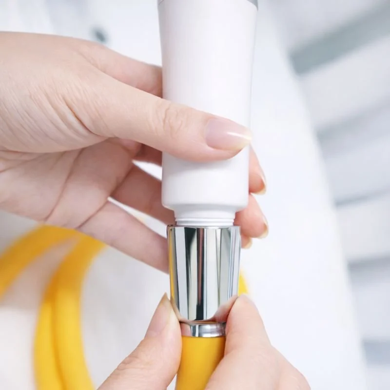 Person squeezing a white tube of lotion or cream onto a yellow-handled applicator.