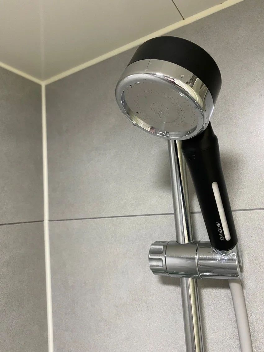 Shower head with a black handle and metallic finish mounted on a tiled bathroom wall.
