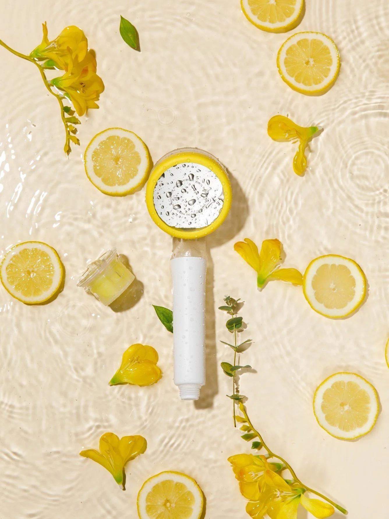 A lemon squeezer with lemon slices, lemon blossoms, and green leaves surrounding it on a water surface.