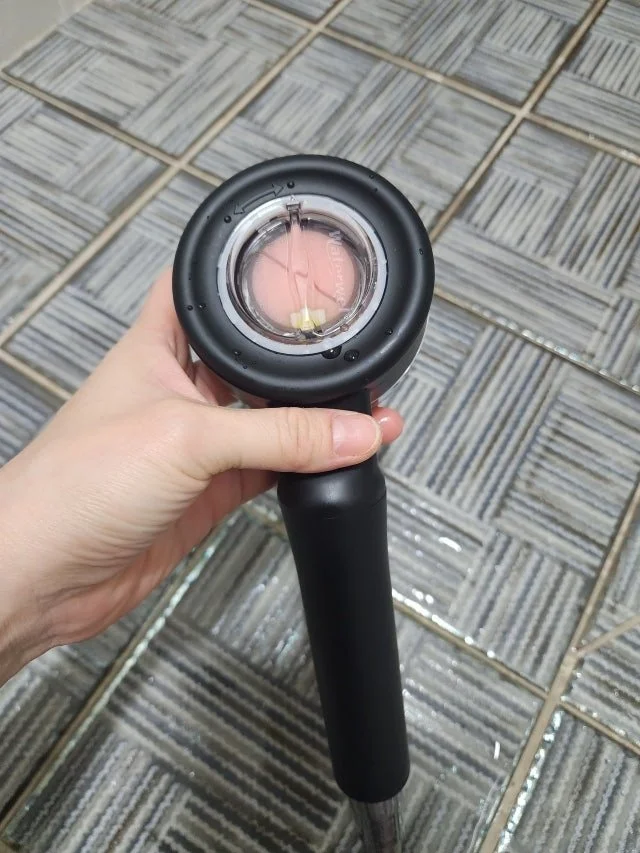 A hand holding a black pool cleaning tool with a transparent suction head, on a tiled floor.