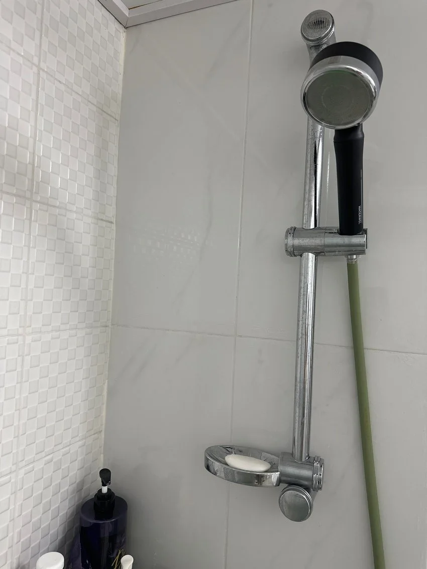 Showerhead and handheld shower on a tiled bathroom wall, with soap on a metal soap dish and bottles on the corner shelf.
