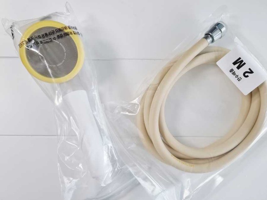 A coiled white shower hose with a chrome connector and a roll of yellow tape in plastic packaging on a white surface.
