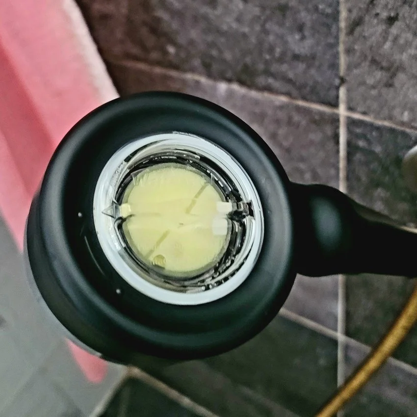 Looking into the opening of a black, LED flashlight, showing the lens and internal LED components. The background has tile and concrete surfaces.