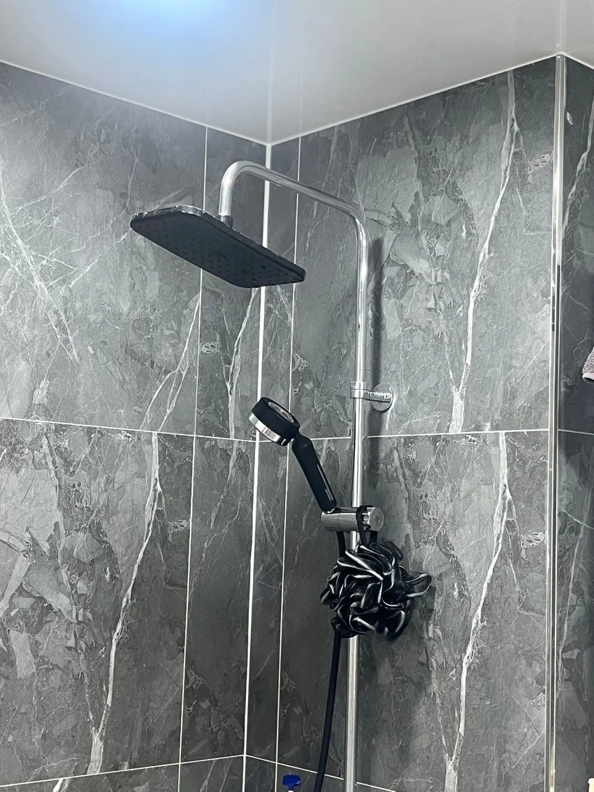 A modern shower with gray marble tiles, a square rain showerhead, and a handheld shower.