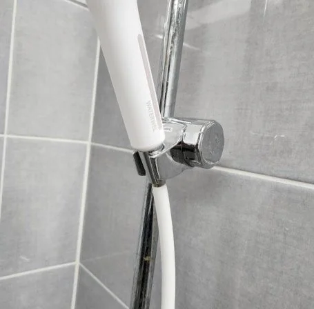 A handheld electric toothbrush attached to a wall-mounted holder in a bathroom with gray tiled wall.
