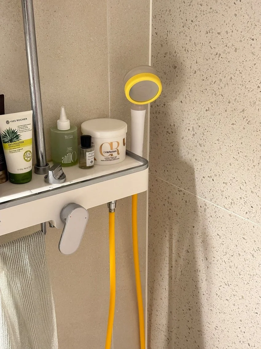 Shelf with skincare products, a UV sterilizer, and two yellow hoses in a shower or bathroom.