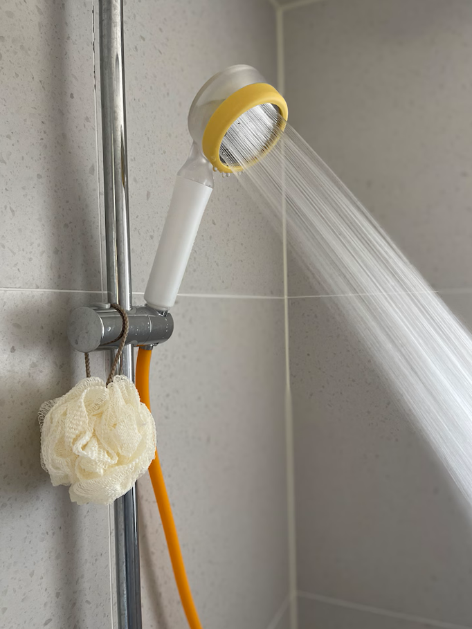 Showerhead attached to a pipe on a tiled wall, water running from it, with a bath sponge hanging below.