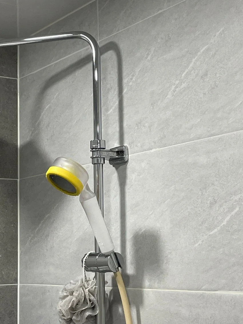 A shower corner with a metal shower rail, a yellow and gray showerhead, and a white shower brush hanging from the rail.