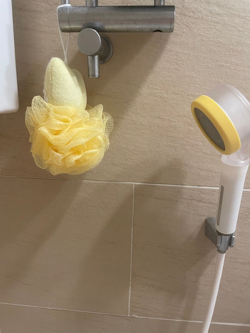 Bathroom wall with yellow bath sponge and showerhead.