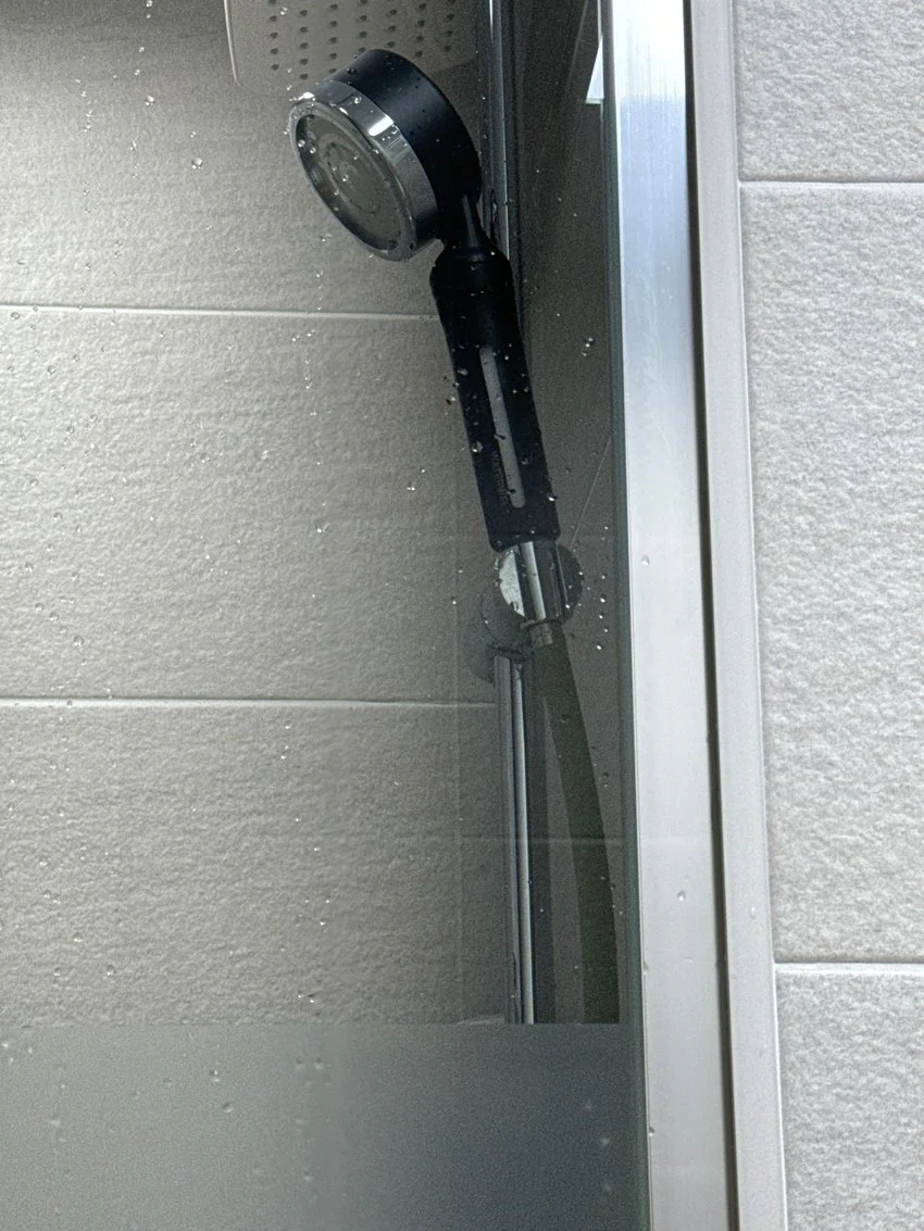 A close-up of a modern outdoor shower head mounted on a wall with water droplets around it.